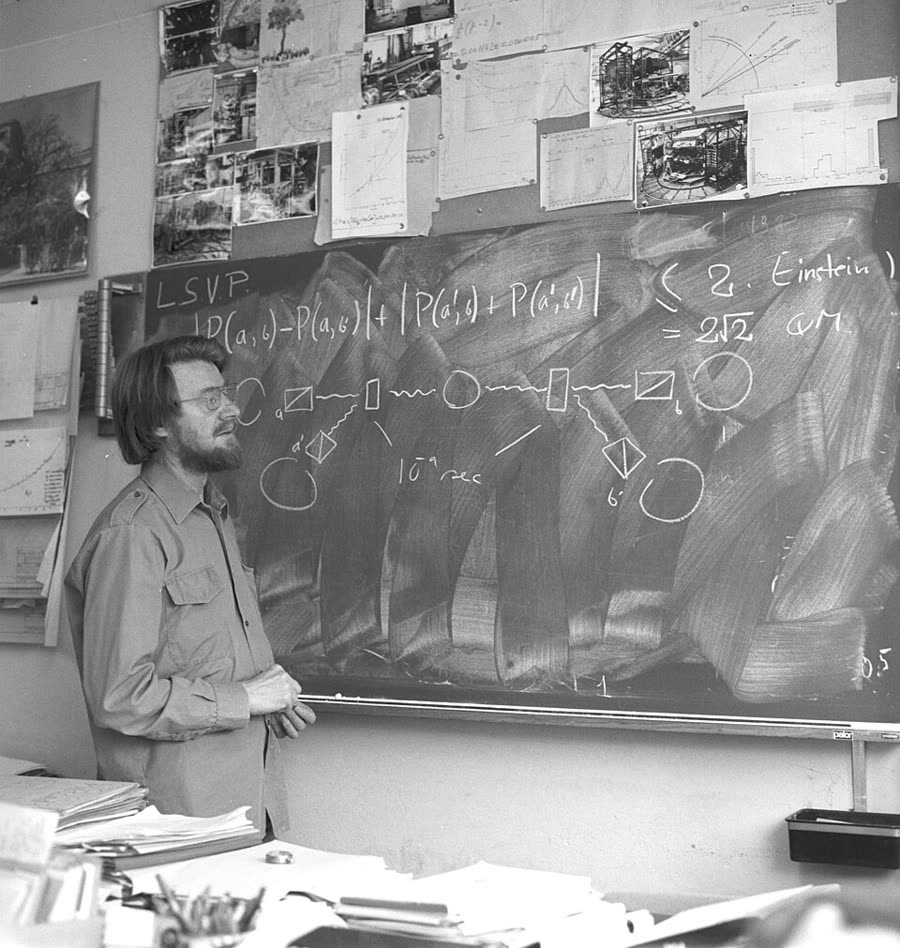 John Bell at a blackboard, gesturing towards written mathematics.