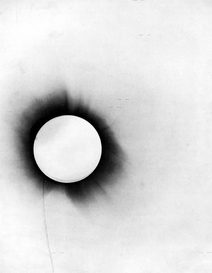 A negative photographic plate of the 1919 total solar eclipse, the dark solar disc surrounded by the corona, with short horizontal marks indicating the measured stars.