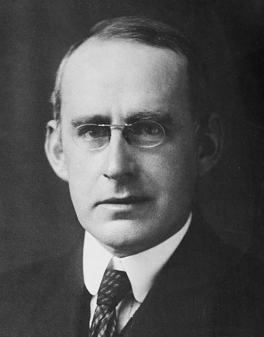 Portrait photograph of Arthur Stanley Eddington in a suit and round spectacles.