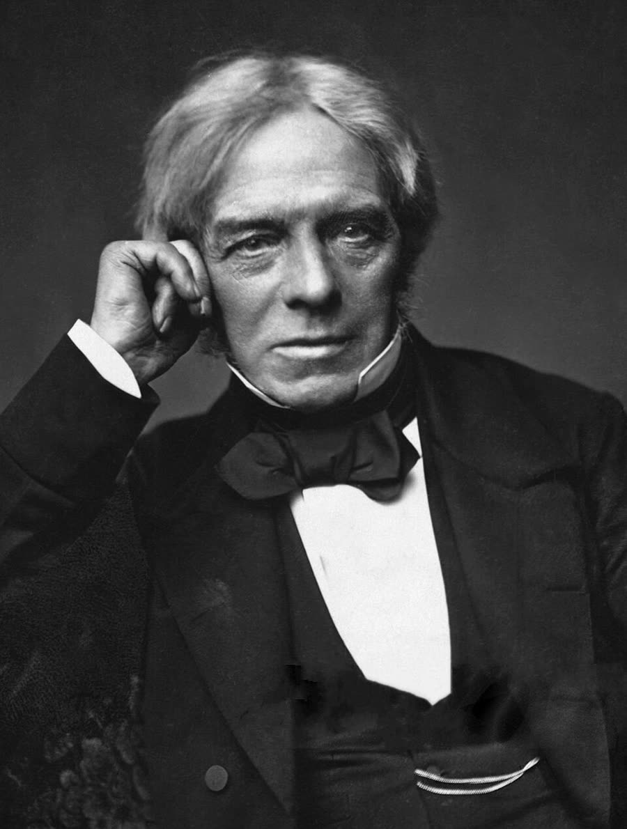 Photographic portrait of Michael Faraday seated, in dark Victorian dress, hands folded.