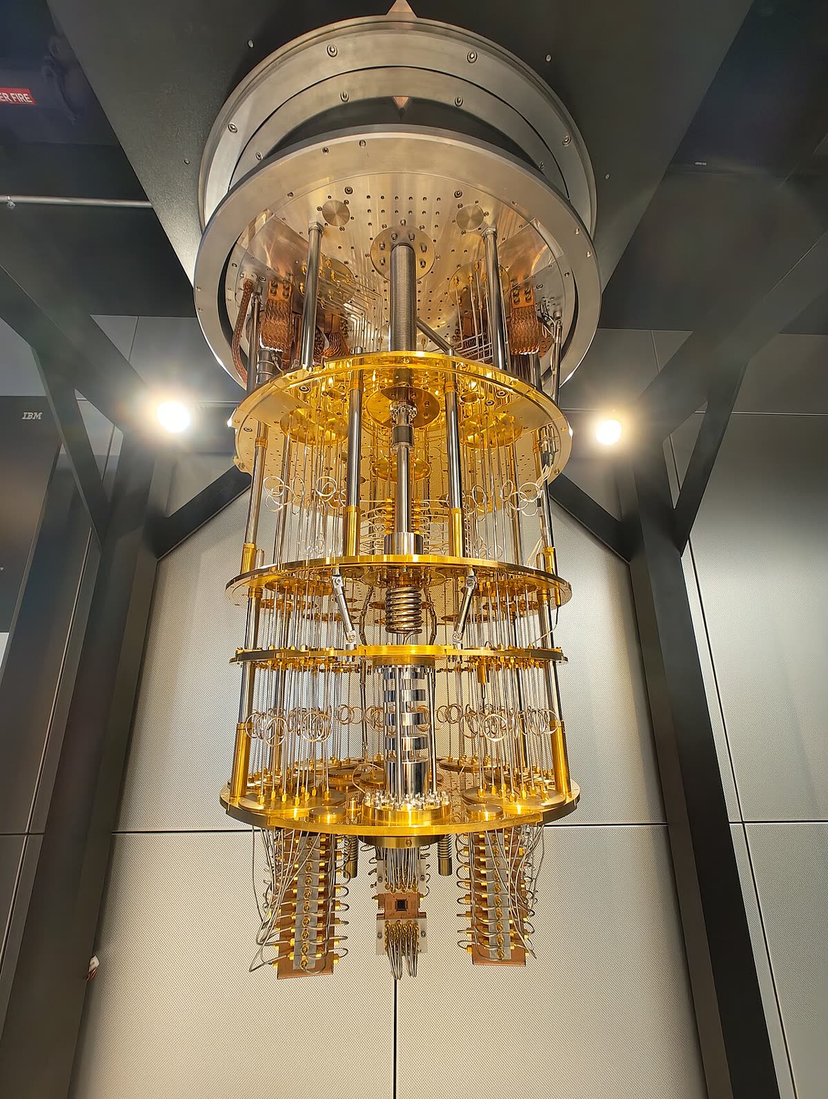 IBM Quantum System One: a chandelier of gold-coloured wiring stages suspended inside a glass case.