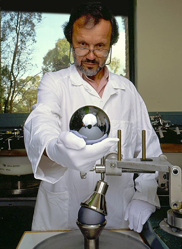 A mirror-polished silicon sphere held in a mount, reflecting the room around it.