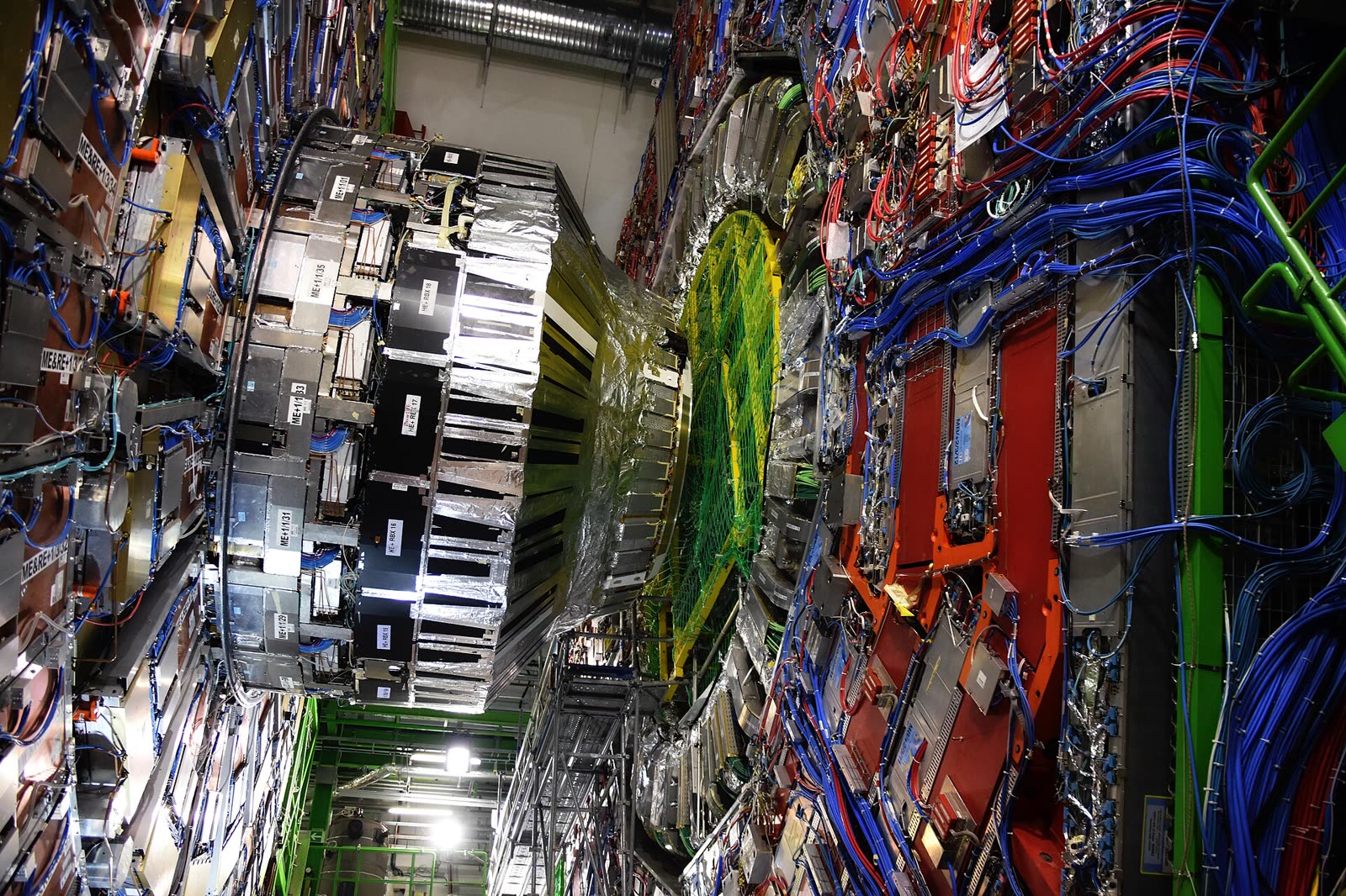 The CMS detector at CERN, a vast cylindrical instrument in red and silver, with people at its base for scale.